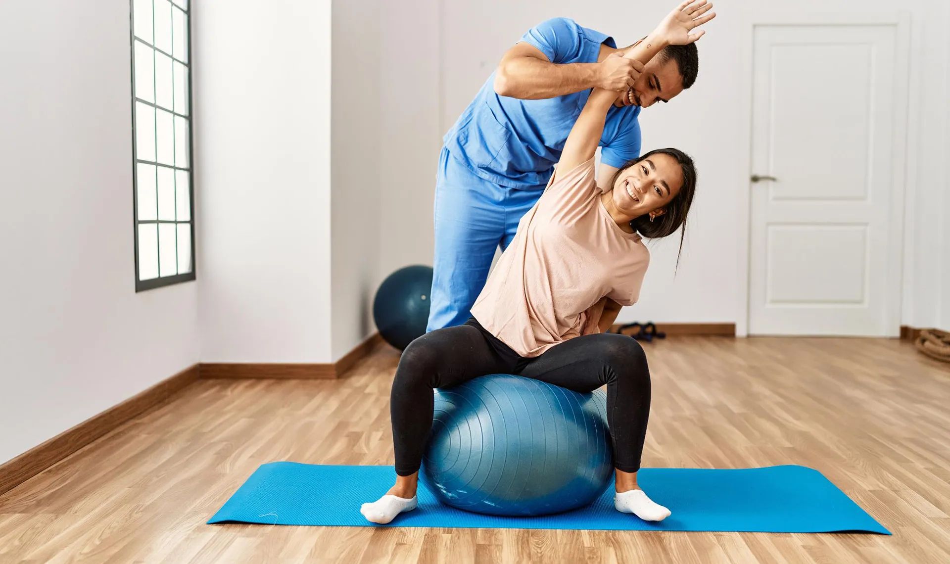 Bewegungstherapie im Reha-Zentrum PV ZAR Graz &ndash; Physiotherapeut unterst&uuml;tzt Patientin bei Dehn&uuml;bung auf Gymnastikball